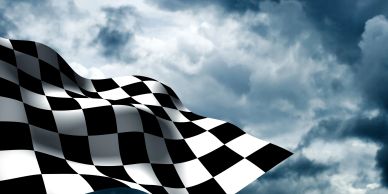 Checkered racing flag waving against a cloudy sky.